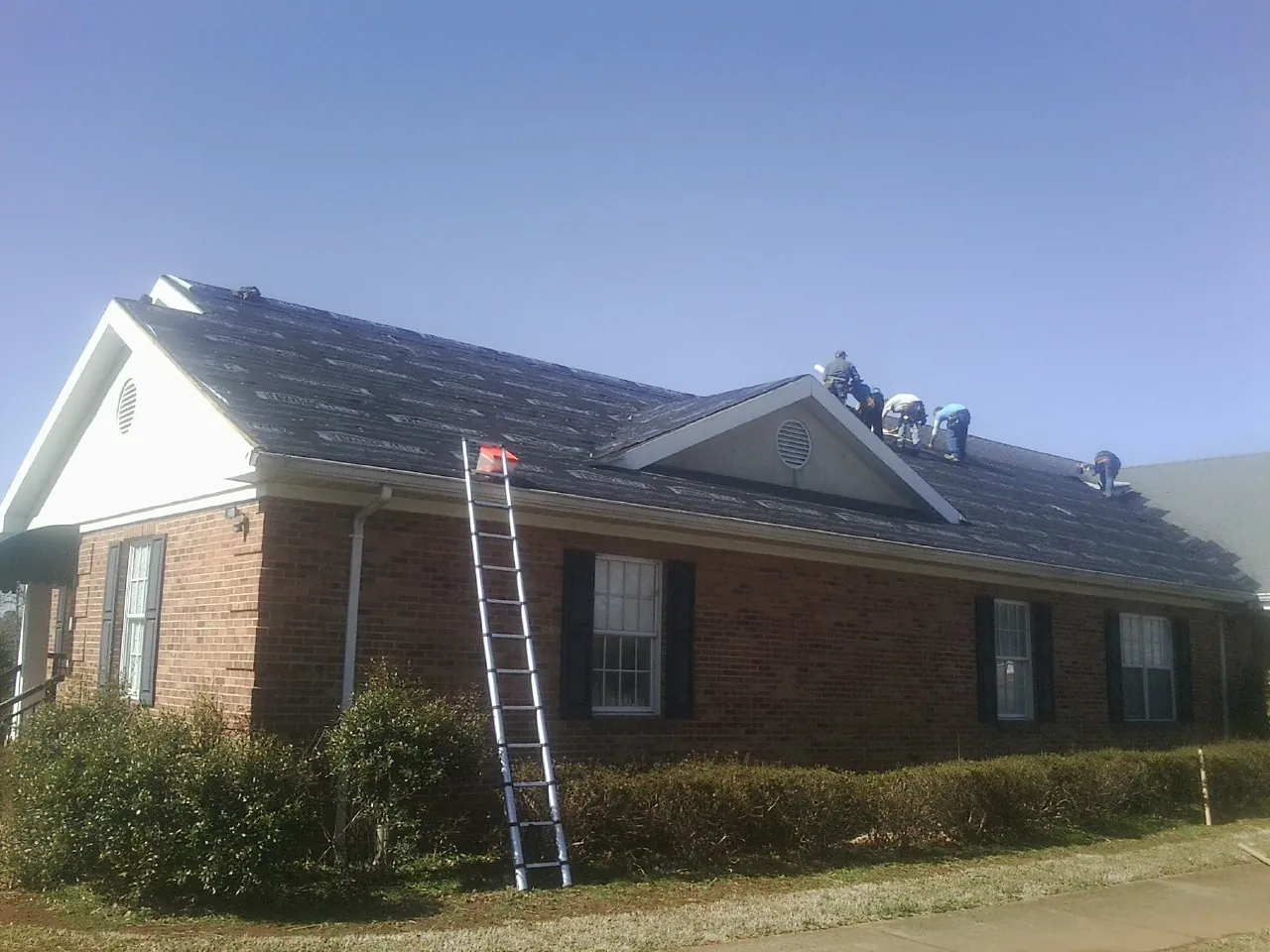 Crew tearing shingles off a brick ranch roof with a ladder set — Emergency Roof Repair work by our crew in Cairo