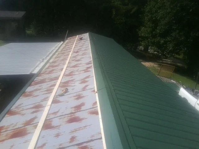 Old rusted panels beside newly installed green metal roofing — Wind Damage Roof Repair by Roofing Brothers in Cairo